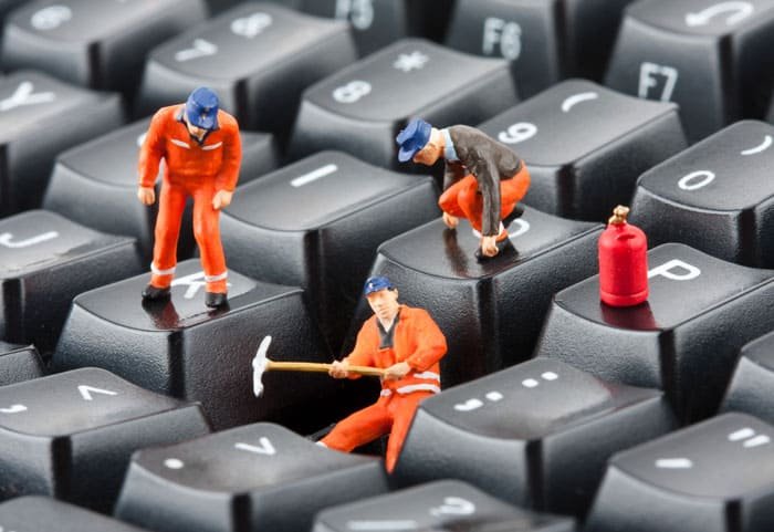 Miniaturas de trabalhadores realizando manutenção simbólica sobre um teclado, representando suporte técnico e manutenção de site